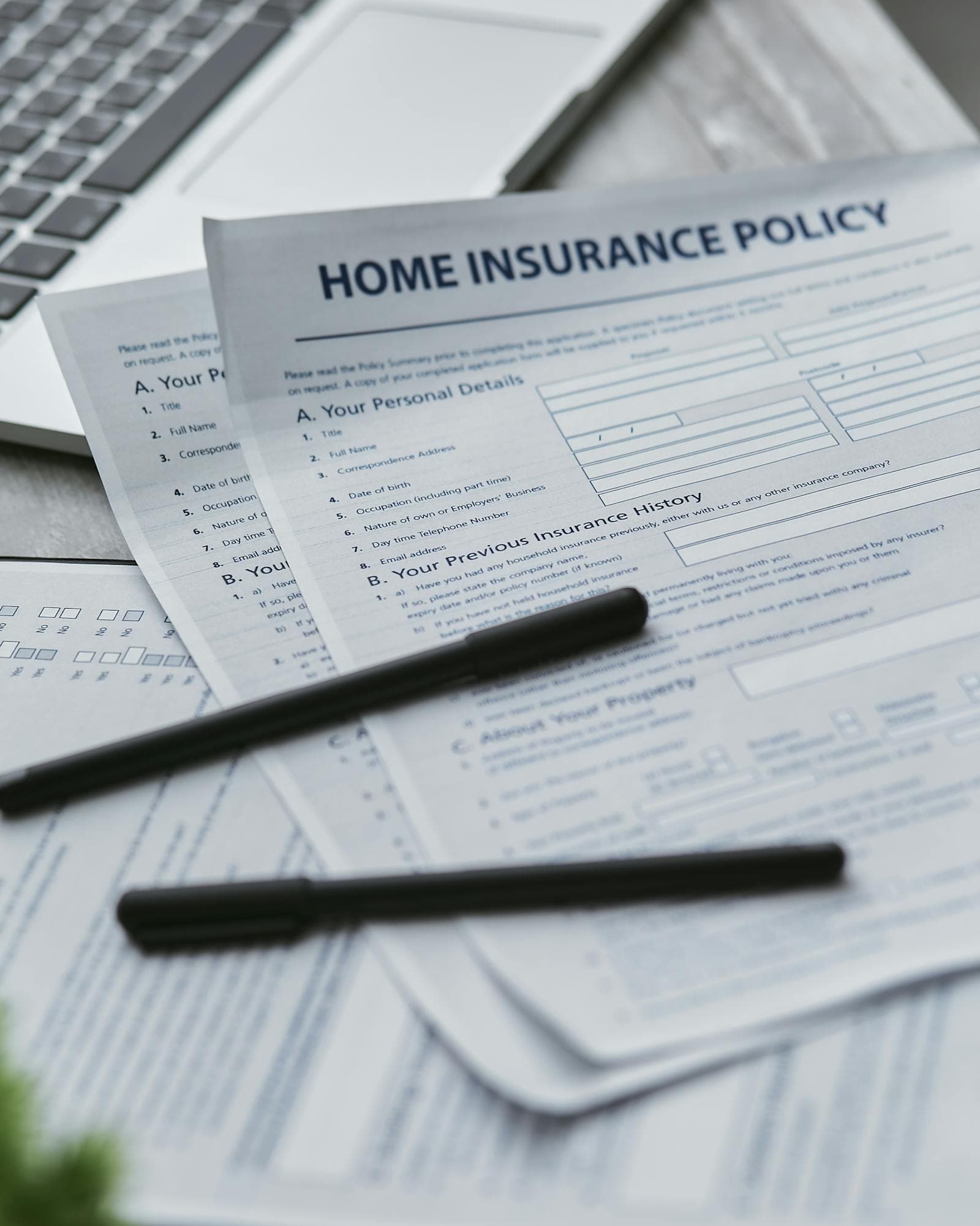 Home insurance policy paperwork on a desk with pens and a laptop